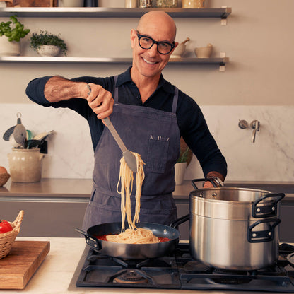 Man in glasses and apron serves pasta from stainless steel Stanley Tucci nonstick frypan.