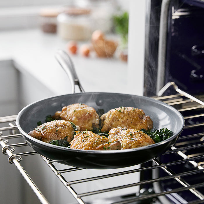 Ceramic nonstick 8-inch frypan with cooked chicken thighs on an open oven rack in a bright kitchen.