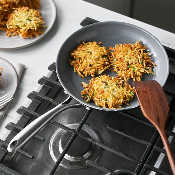 Three hash browns in a Swift ceramic nonstick 8-inch frypan on a gas stove with a wooden spatula beside it.