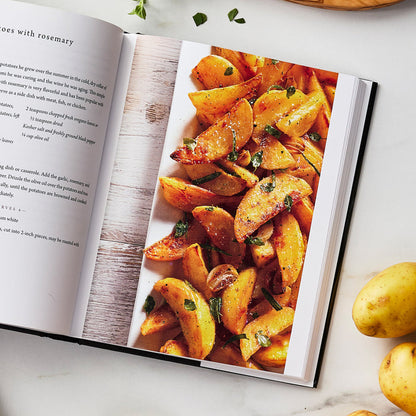 The Tucci Cookbook displayed open, showing a recipe page with golden roasted potato wedges topped with herbs.