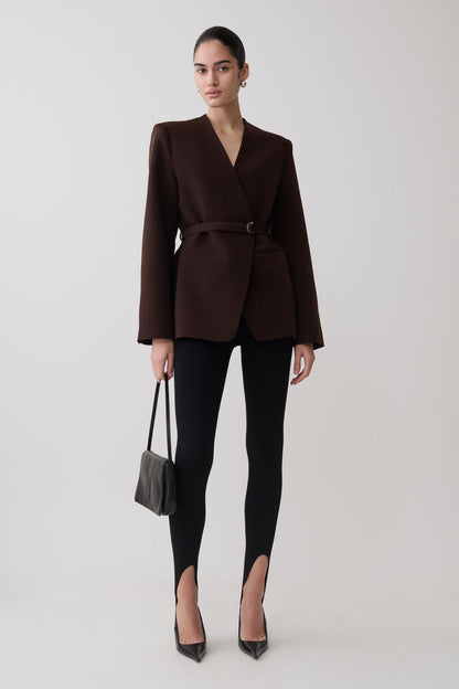 Woman wearing a brown blazer and knit black leggings.