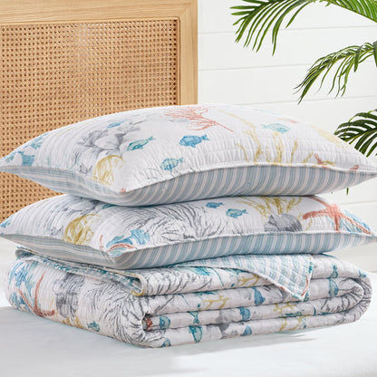 Stack of floral-patterned pillows and quilt on a bed with a wooden headboard and plant leaves.